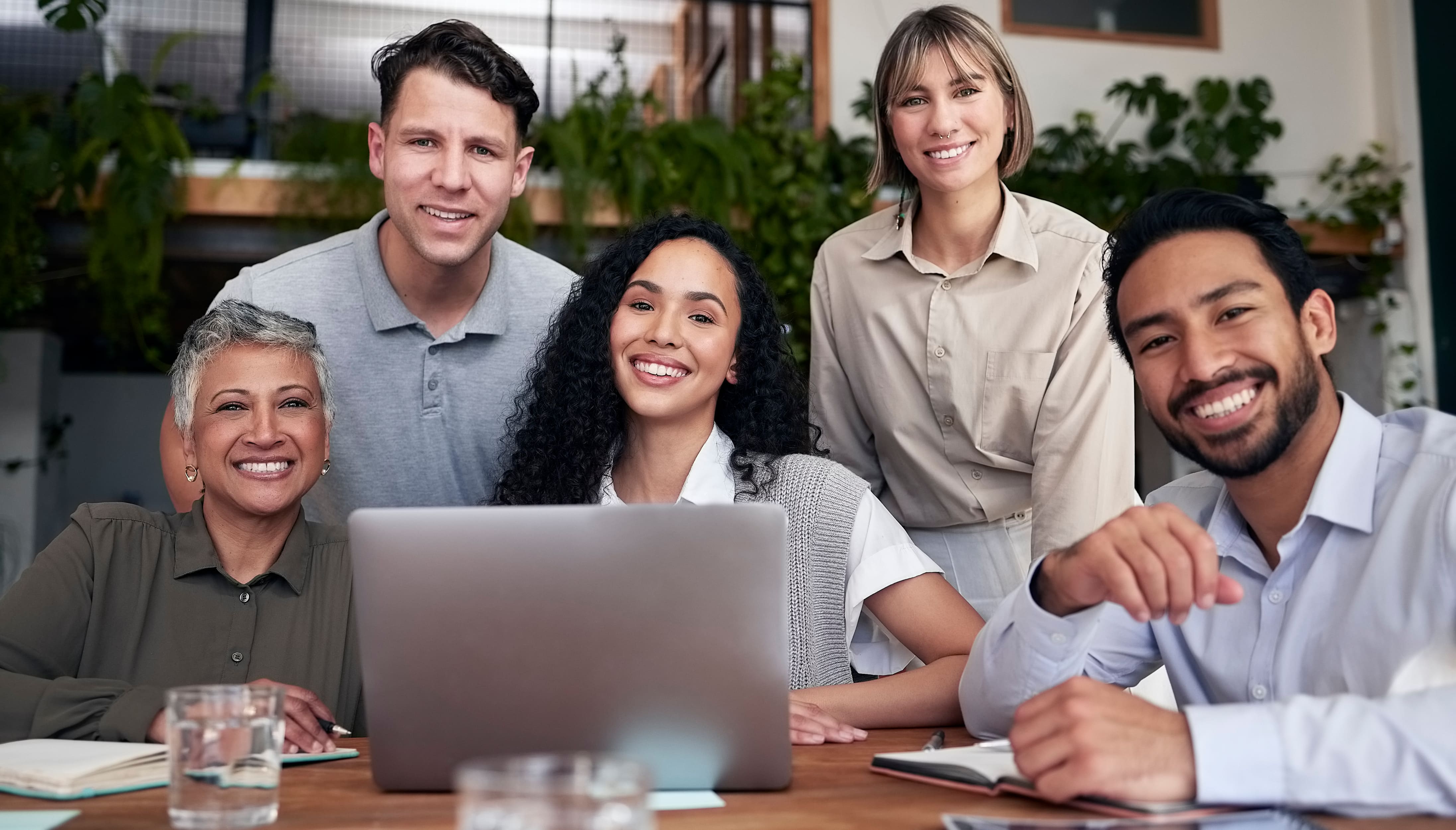 A smiling team of colleagues gathered around a laptop