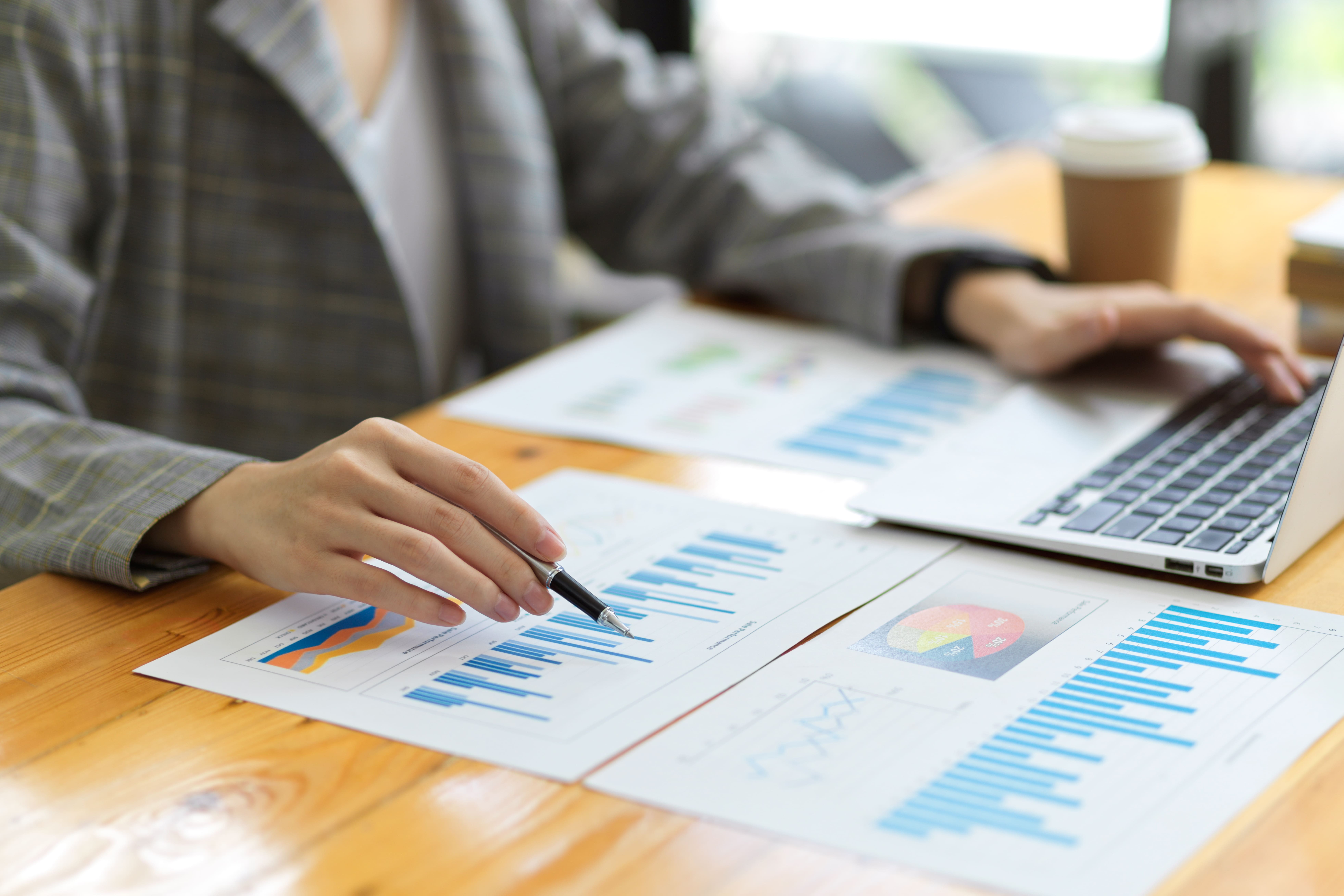 Hands reviewing charts and reports on a desk with a laptop